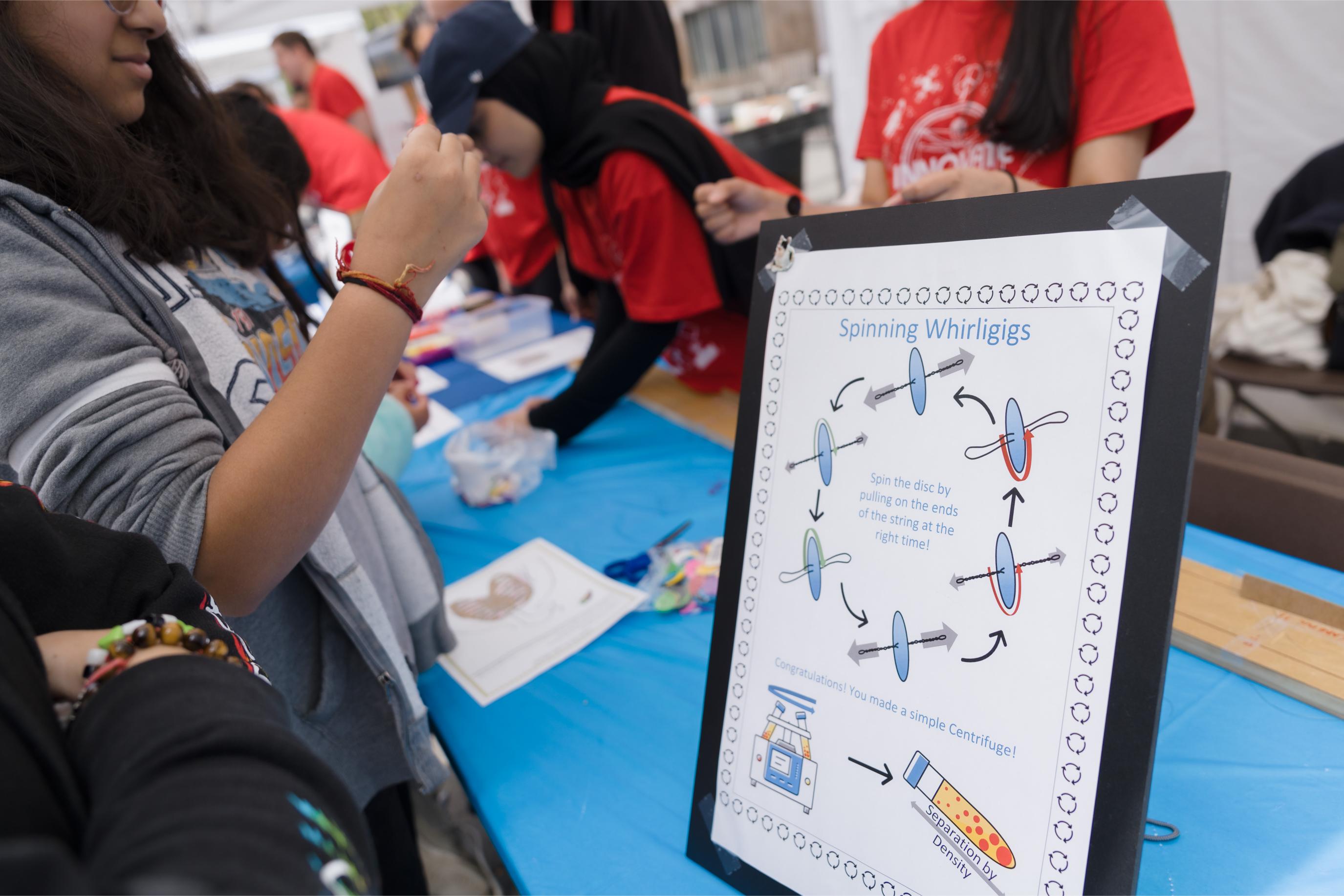 A presentation board showing how to play with spinning whirligigs at the Fun with Physics Booth.